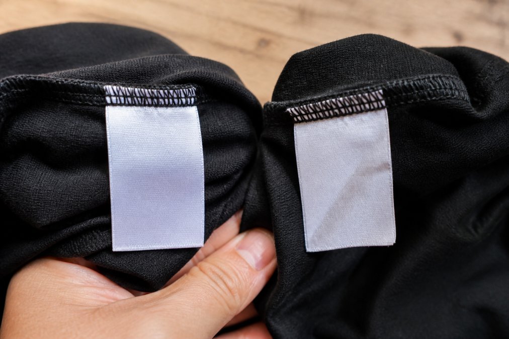 Close-up of a genuine branded garment label next to a counterfeit version showing clear differences in stitching, font clarity and tag quality under natural daylight