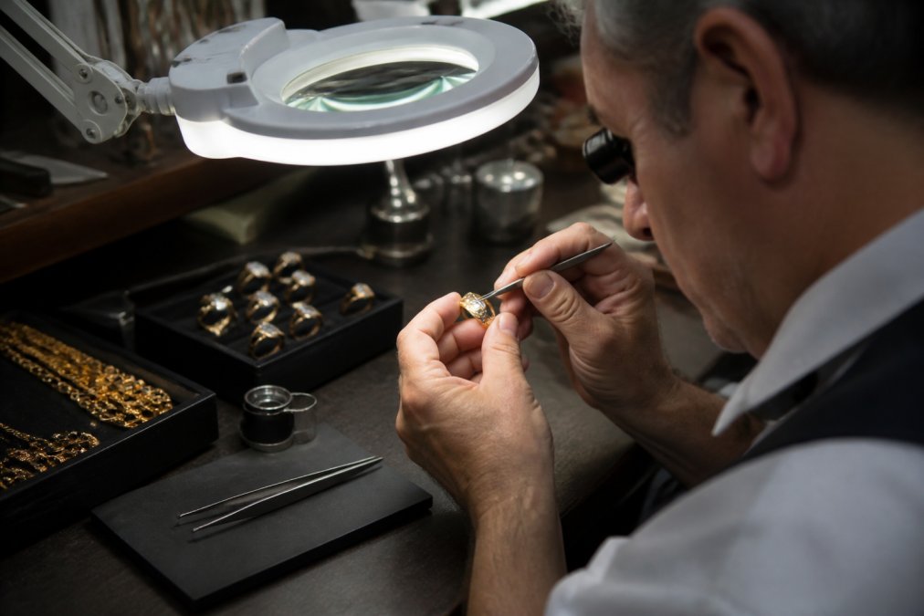 Jeweler using a magnifying loupe to inspect hallmark stamps on a gold ring under a bright lamp