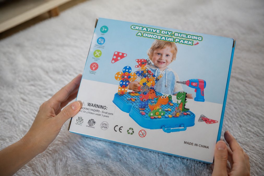 Parent hands examining a toy package, looking at safety labels, certification marks, and product information on the back in natural light