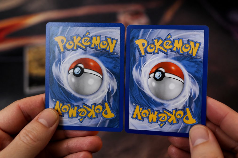 Close-up of hands comparing authentic and counterfeit Pokémon card surfaces, showing texture differences and card stock quality under natural lighting