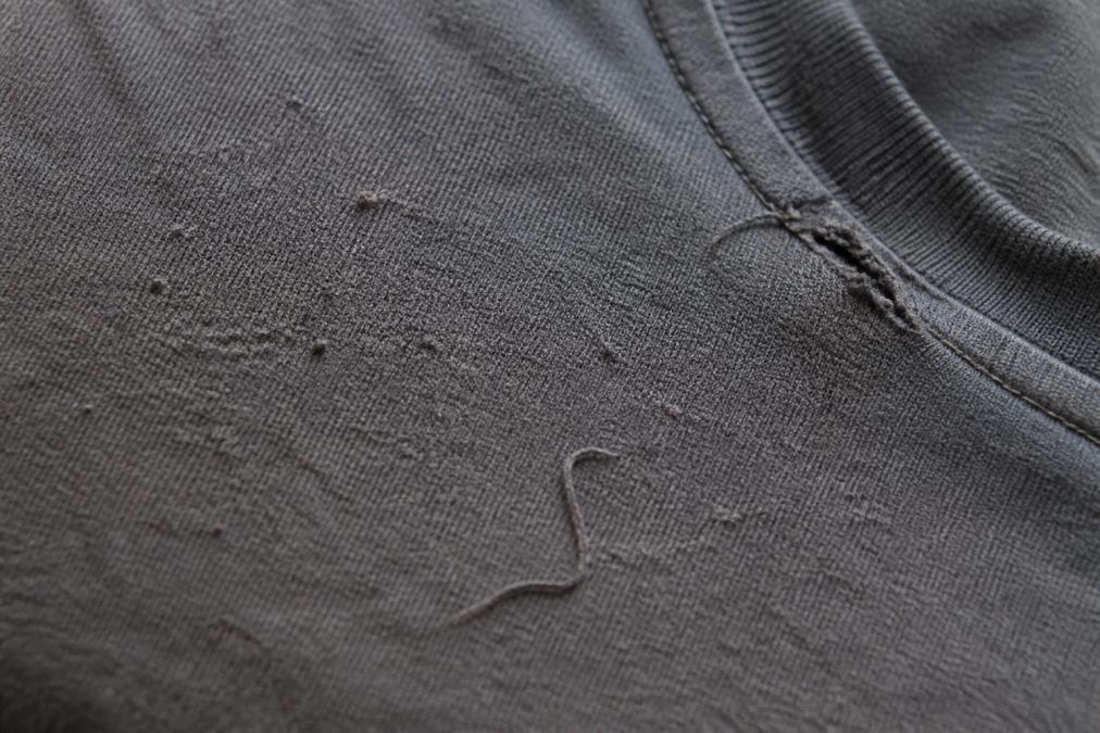 Detailed view of fabric showing pilling, loose threads, and visible construction flaws on a worn t-shirt under natural light