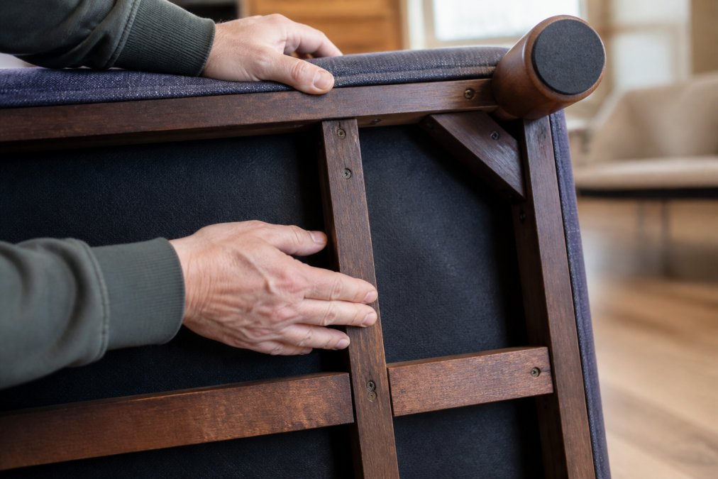 Close-up of hands examining the wooden frame and reinforced joints underneath a pet bed, checking construction quality and stability