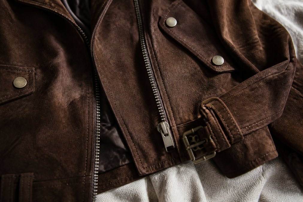 Close-up of quality metal zipper, decorative buttons, and hardware on trendy garment laid flat on fabric surface with natural side lighting