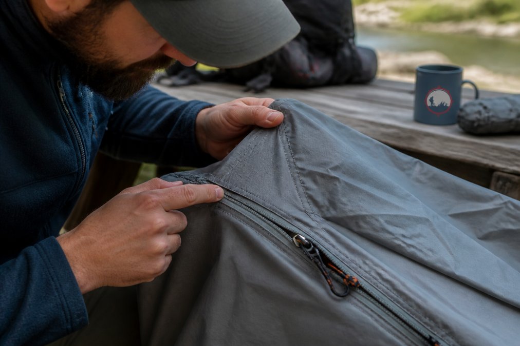 Close-up of hands carefully examining tent seam stitching and zipper mechanisms, demonstrating tactile inspection of stitching quality and hardware integrity under natural lighting