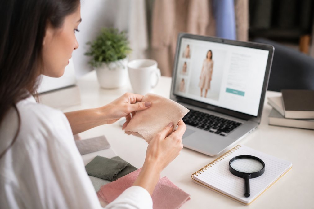 Hands holding a fabric swatch near a laptop to spot quality clothing before making an online purchase