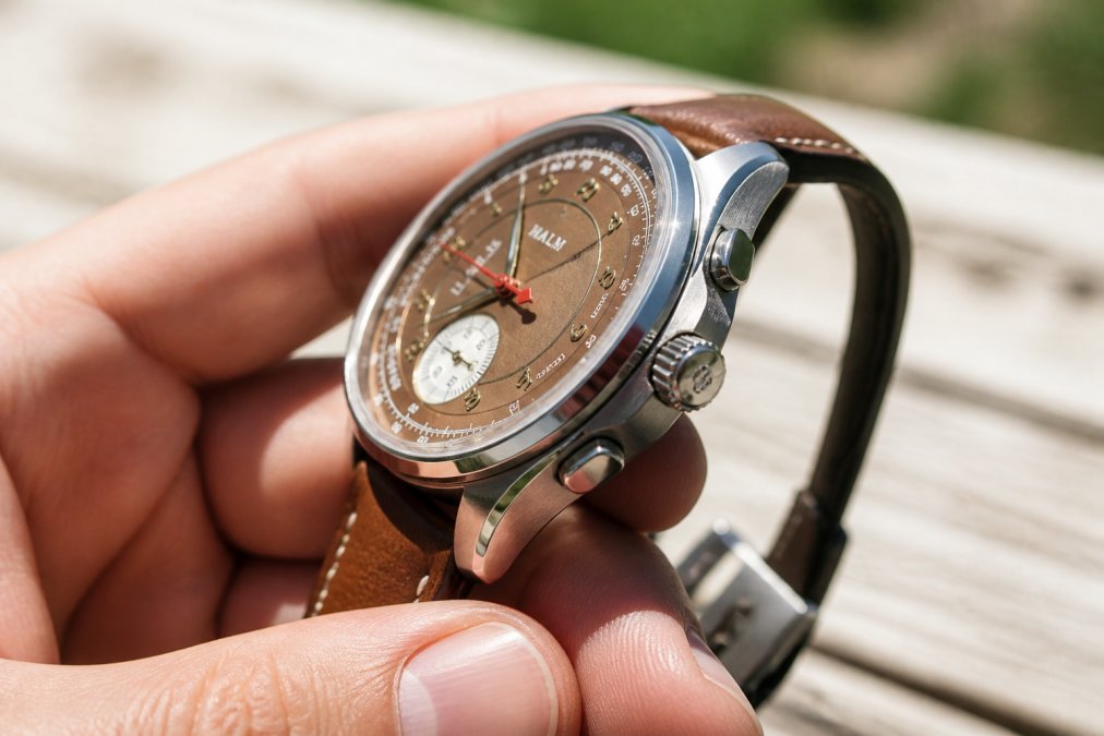 Close-up of a hand holding a watch under bright natural light, showing polished and brushed case surfaces with visible chamfered edges catching light at different angles