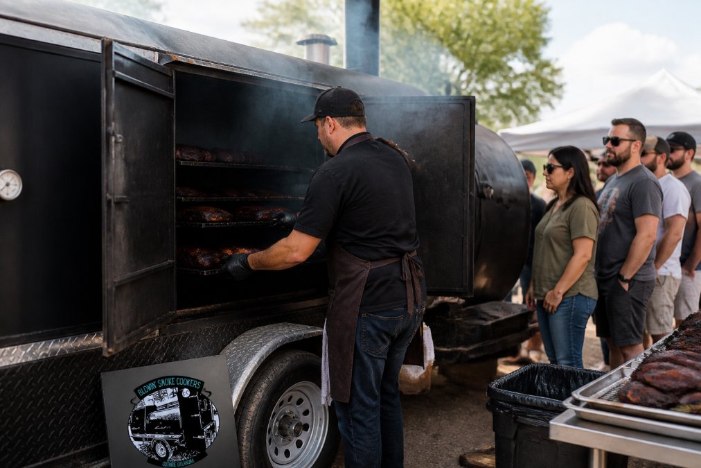 Pitmaster loading brisket into a commercial smoker at a BBQ catering event