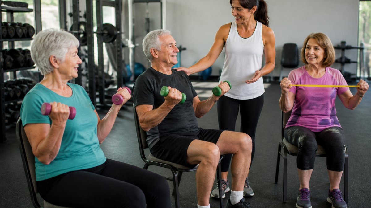 Friendly instructor guiding seniors working out at 60 with dumbbells and resistance bands in a bright gym.