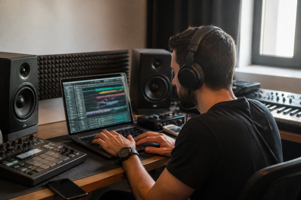 Music producer working at studio setup with headphones and equipment, reviewing tracks on a laptop screen in modern production environment