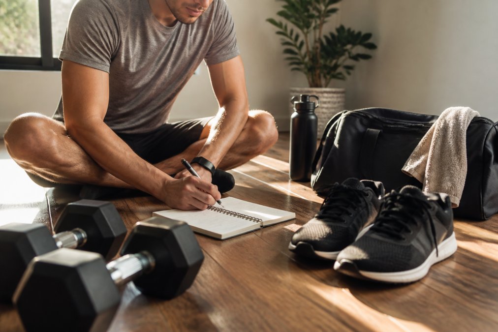 Workout log and training shoes laid out on a floor to help you learn how to stay consistent with lifting