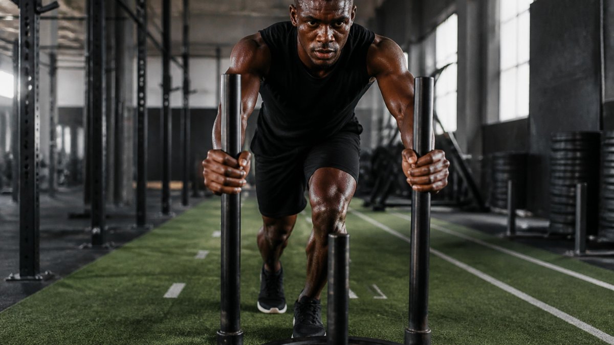 Athlete in Krush Khaos apparel training intensely in gym with focused determination, sweat visible on face and body, performing high-intensity exercise with strong posture and concentration