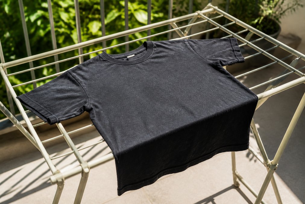 A graphic tee laid flat on a light-colored drying rack in bright natural sunlight, showing proper air-drying technique with the graphic facing up