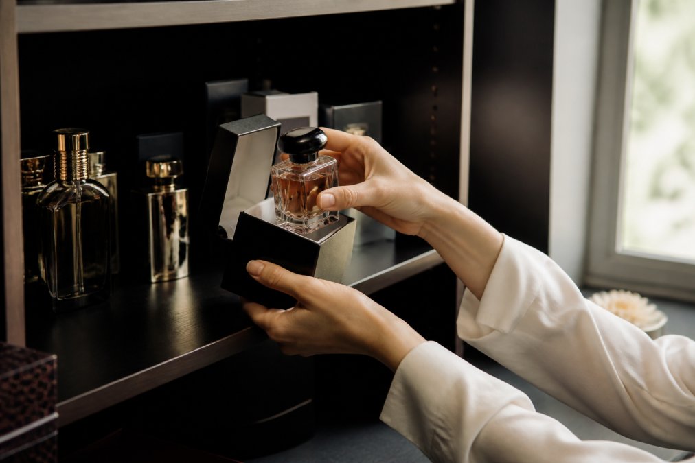 Hands placing a bottle into its box to store designer perfume in a cool, dark cabinet away from direct light.