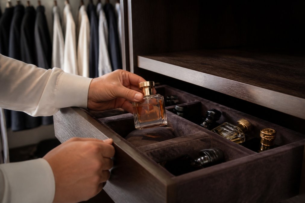 Person placing a glass perfume bottle into a dark wooden drawer to store expensive perfume away from light