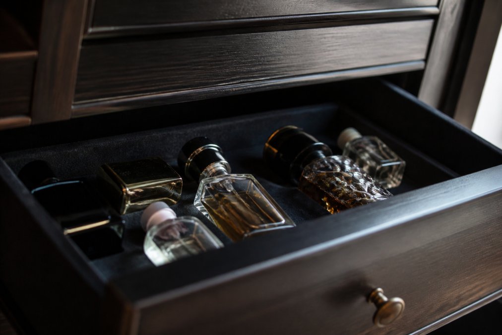 Perfume bottles organized in a velvet-lined wooden drawer to store perfume in a cool, dark environment.