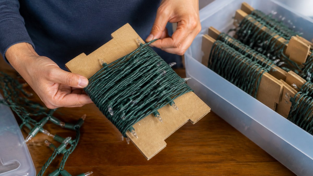 Close-up of hands neatly wrapping Christmas light strings around cardboard in organized coils, showing the tangle-free wrapping method in action with natural lighting