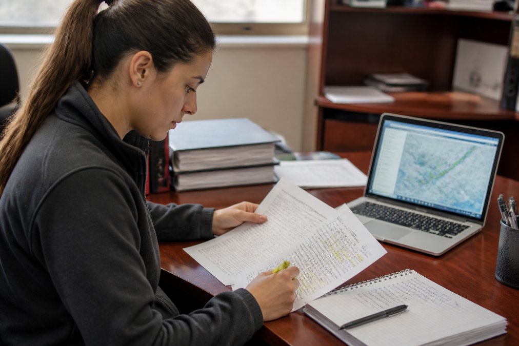 Dispatcher trainee analyzing METAR and TAF reports for dispatcher meteorology training in a bright study room