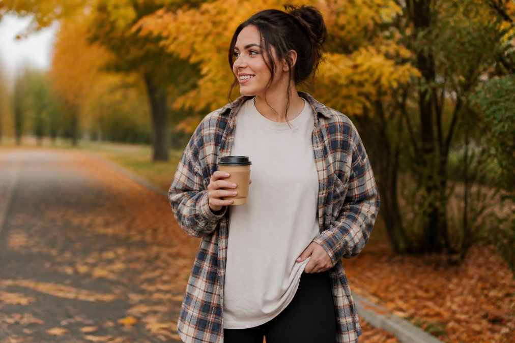 Woman wearing an oversized faith-based graphic tee under an open flannel shirt while holding coffee outdoors.