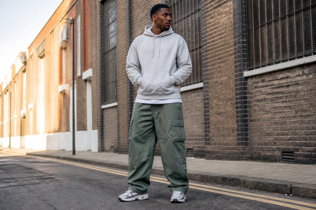 A man wearing wide-leg cargo pants and chunky sneakers, standing on an urban street, full-body shot showing the break of the pant over the shoe