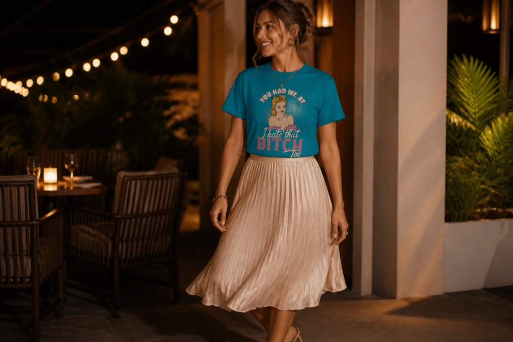 Woman styling a funny graphic tee with a flowing midi skirt, strappy heels, and delicate gold statement jewelry, ready for an evening event with warm ambient lighting