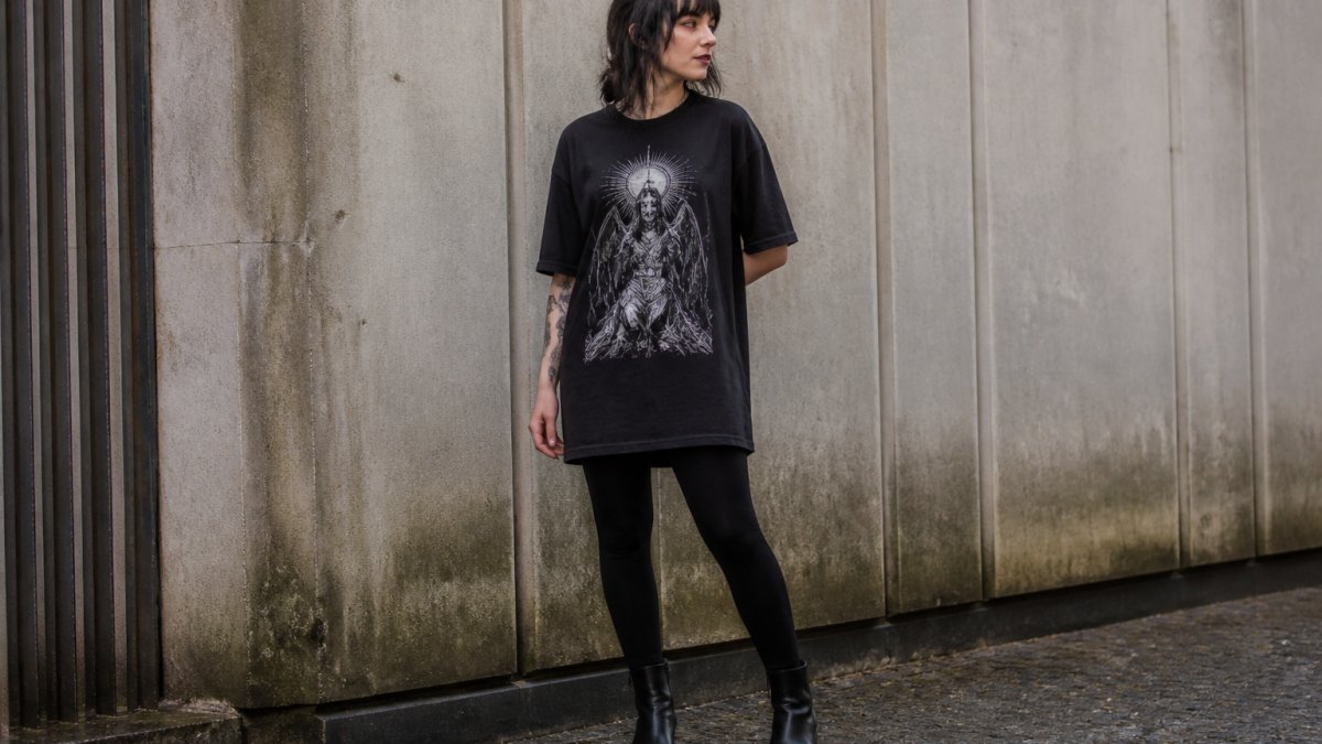 Person wearing an oversized graphic gothic tee with black leggings and ankle boots in natural sunlight