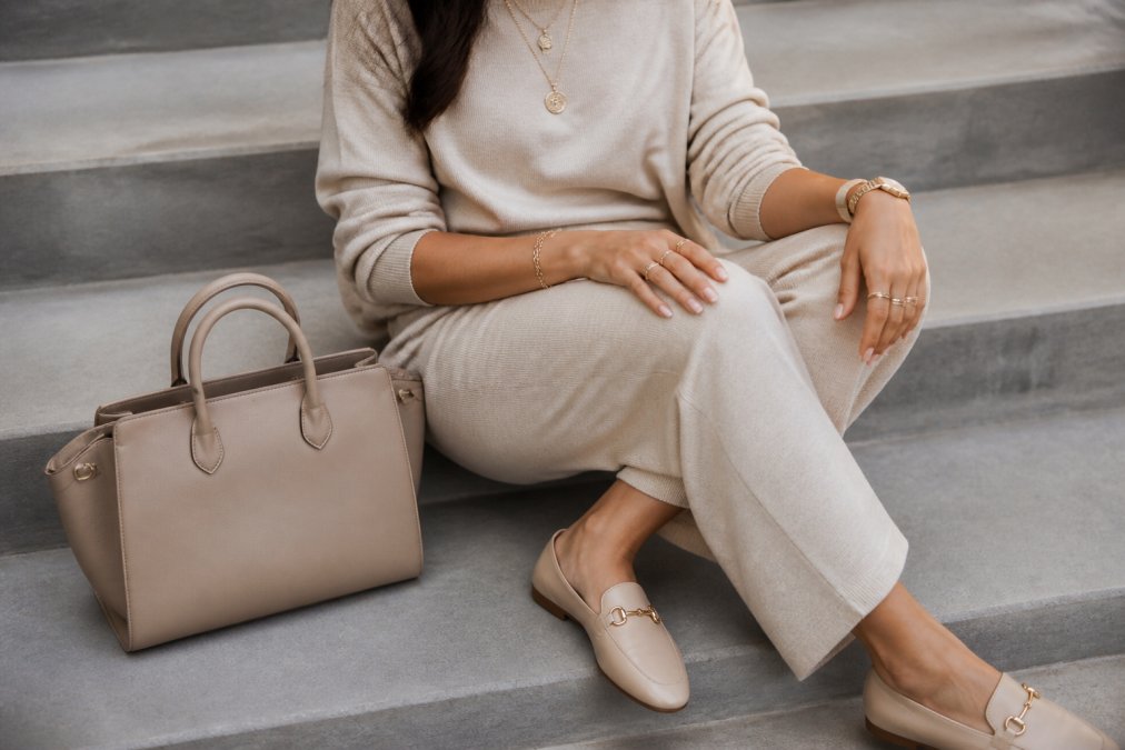 Close-up of a styled loungewear outfit featuring polished accessories: structured handbag, layered jewelry, and professional footwear on a neutral background