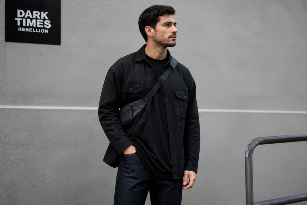 A man wearing a minimalist christian apparel graphic tee layered under an overshirt against an urban wall.
