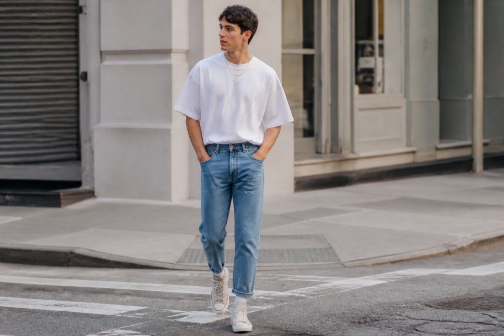 Young man in a white oversized t-shirt tucked into tapered jeans and high-top sneakers on a city street