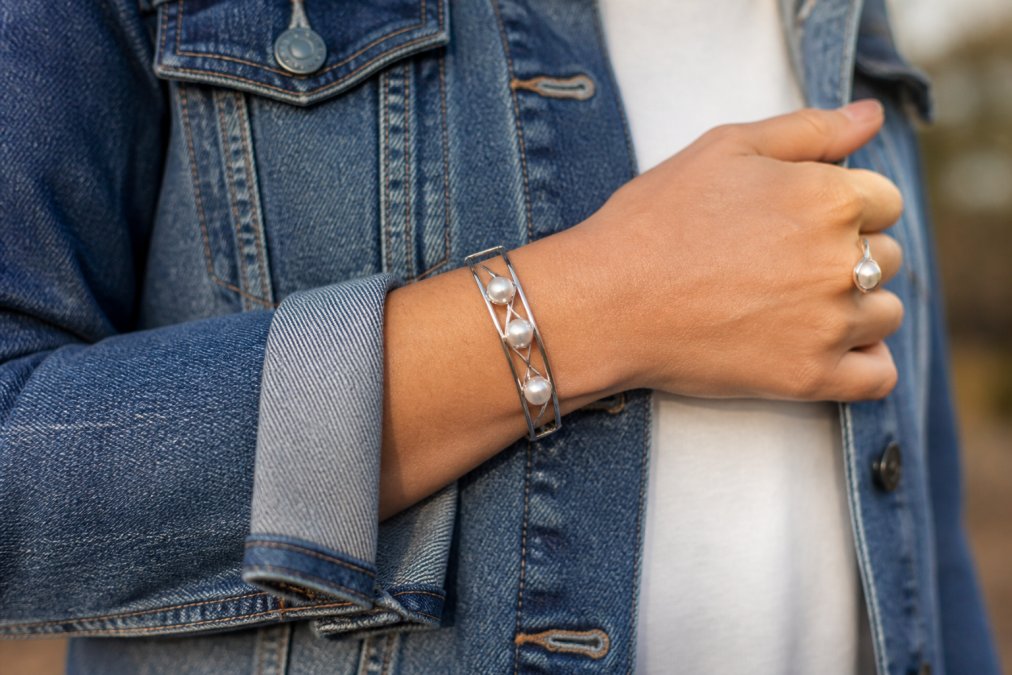 Close-up of a woman's wrist wearing a sterling silver cuff set with round freshwater pearls, styled with a denim jacket sleeve and a simple silver ring, soft natural daylight