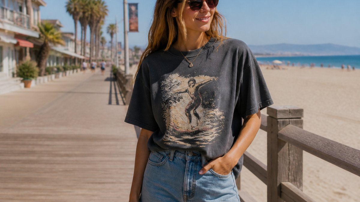 Young adult in an oversized washed graphic tee tucked into denim shorts on a sunny beach boardwalk