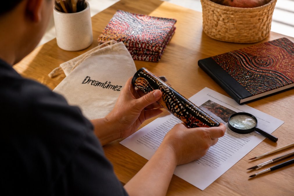 Close-up of hands holding an authentic Indigenous art product, studying artist certification details and cultural documentation with a magnifying glass, natural daylight