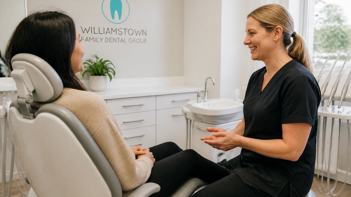 Patient sitting in modern dental chair during consultation with dentist reviewing digital records on computer screen, warm clinical lighting