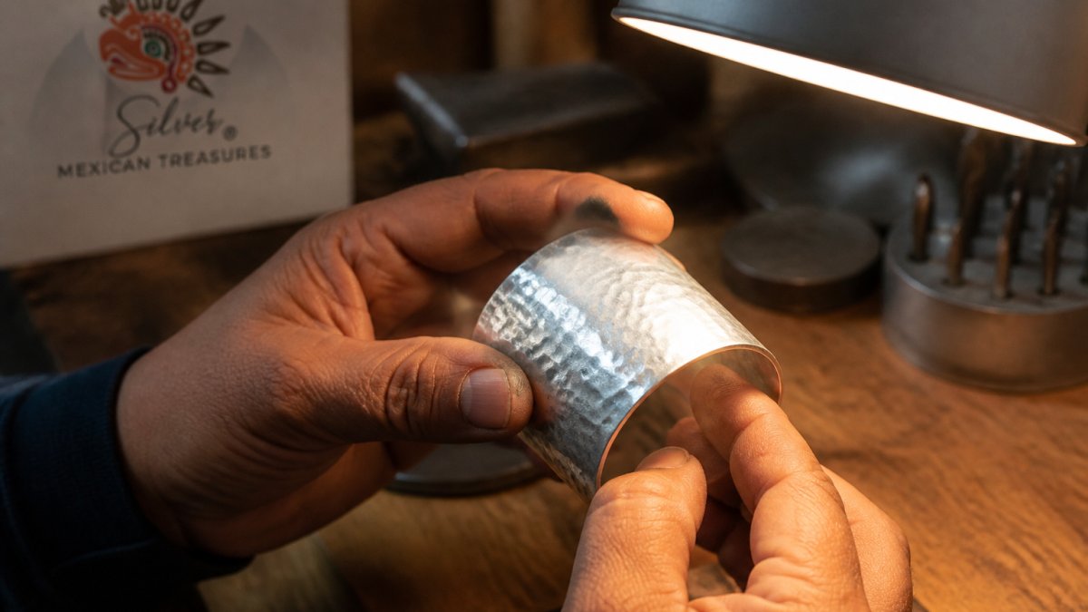Jeweler inspecting a silver bracelet with hammered texture and tool marks under a bright work lamp
