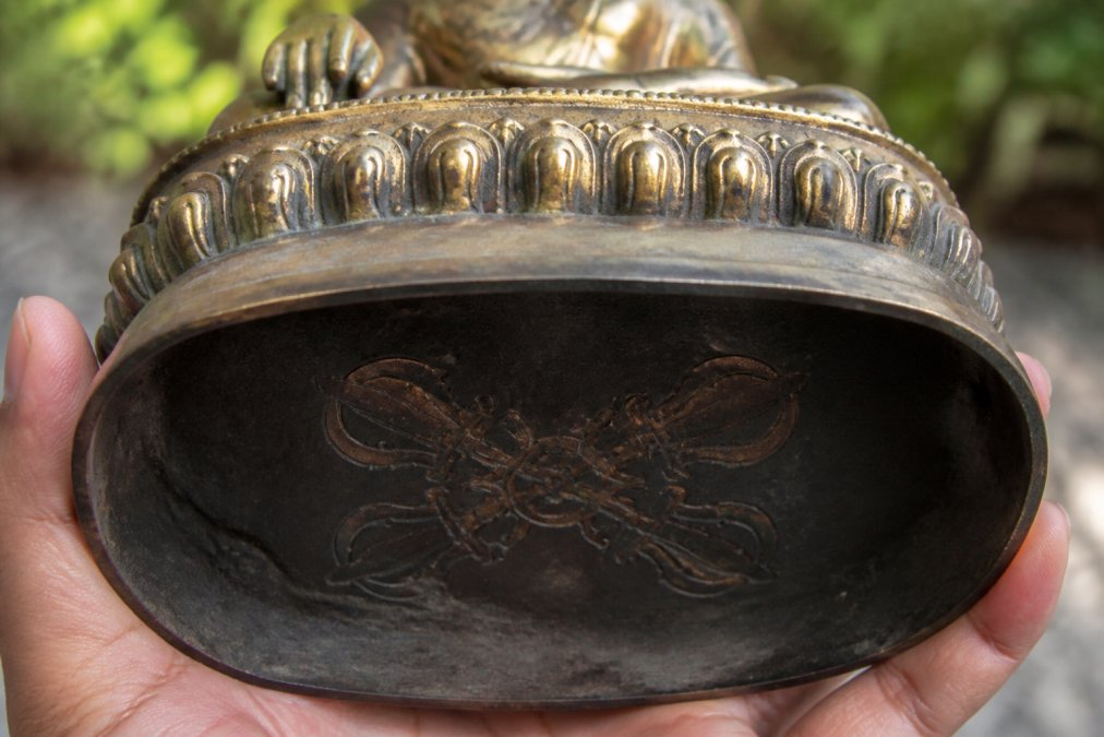 Close-up detail of a Buddha statue's base showing the double vajra seal, base plate, and sacred markings on the underside with natural lighting