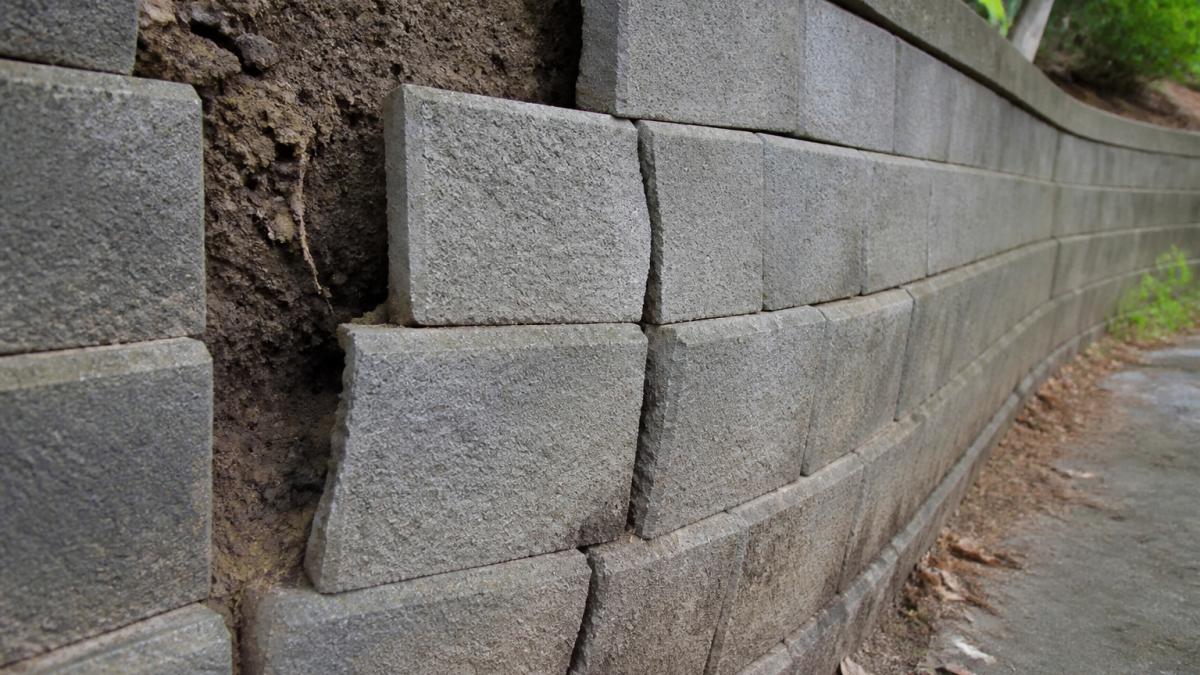 Diagram showing a retaining wall failing with outward block bulging, soil displacement, and structural cracks.