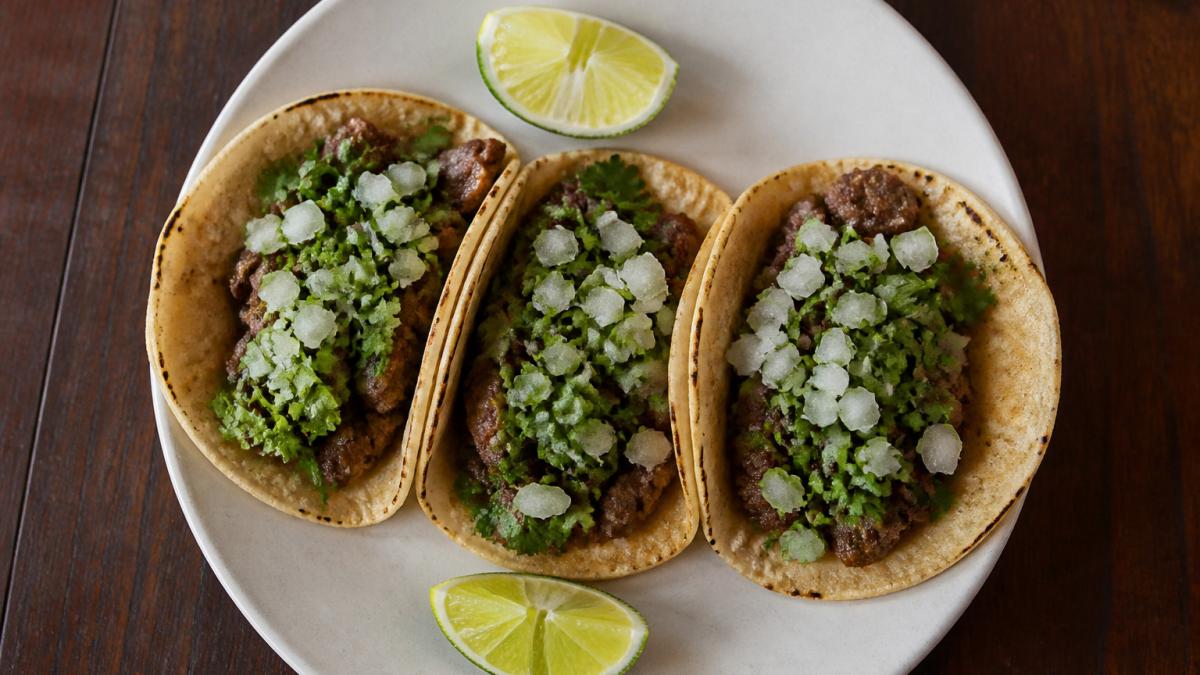 Three authentic tacos served on a ceramic plate with cilantro, diced onion, and fresh lime wedges.