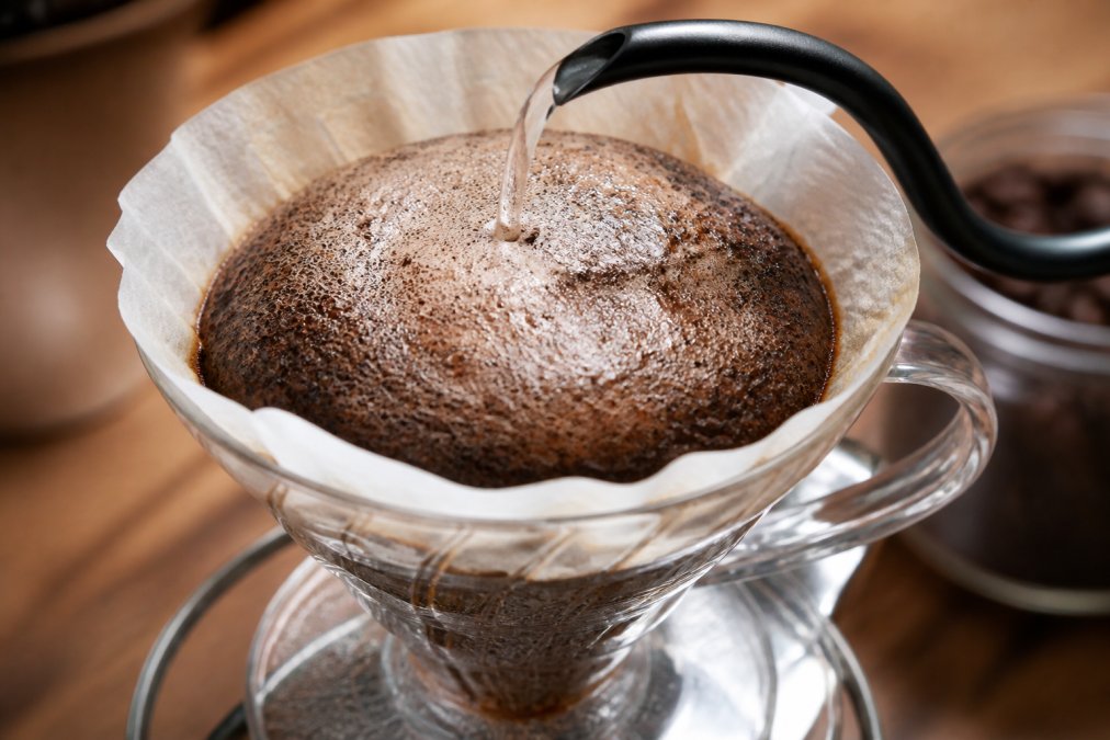 Close-up of a pour-over coffee brewer with hot water hitting fresh coffee grounds, creating a bubbling, blooming dome of foam