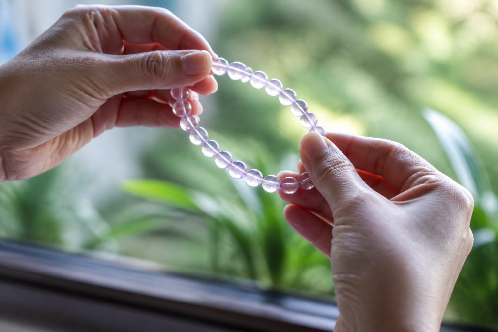 Close-up of a person's hands holding a natural gemstone bracelet up to natural light, examining the beads for colour distribution and internal clarity