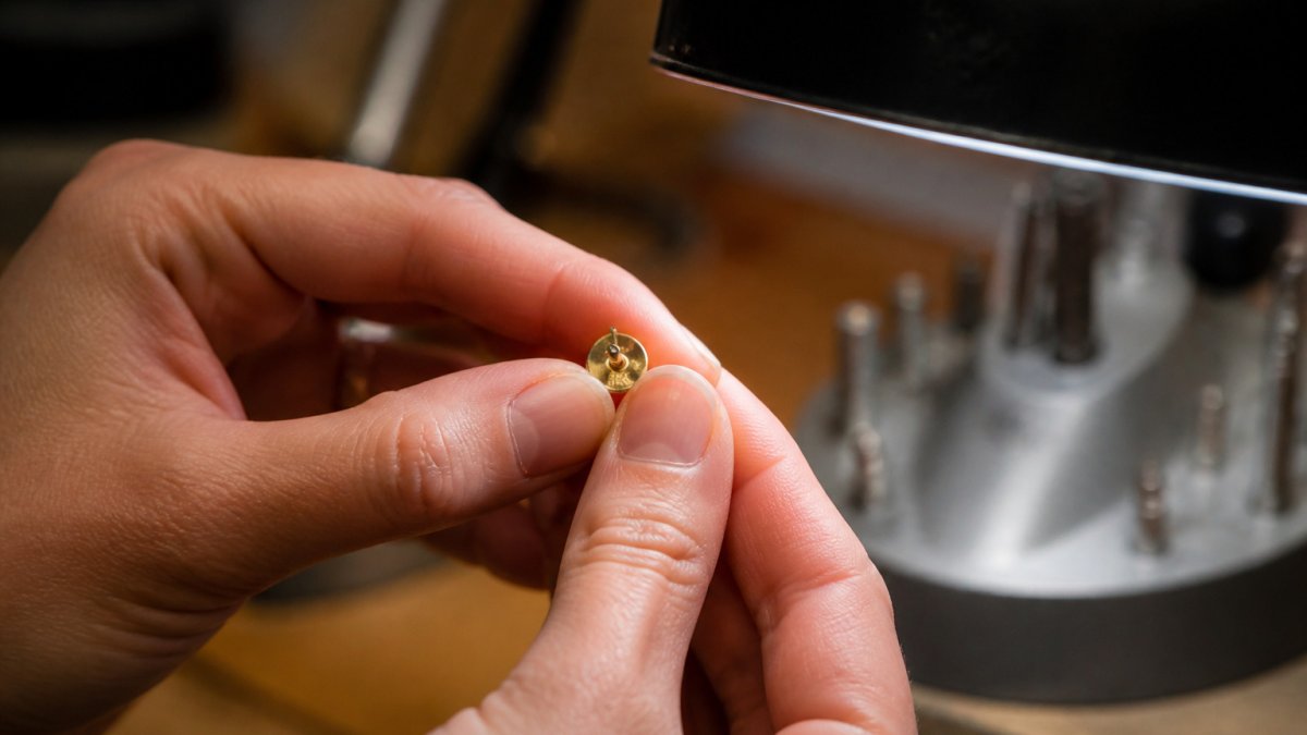 Jeweler holding a 14K gold stud under a bench lamp to inspect the hallmark engraving