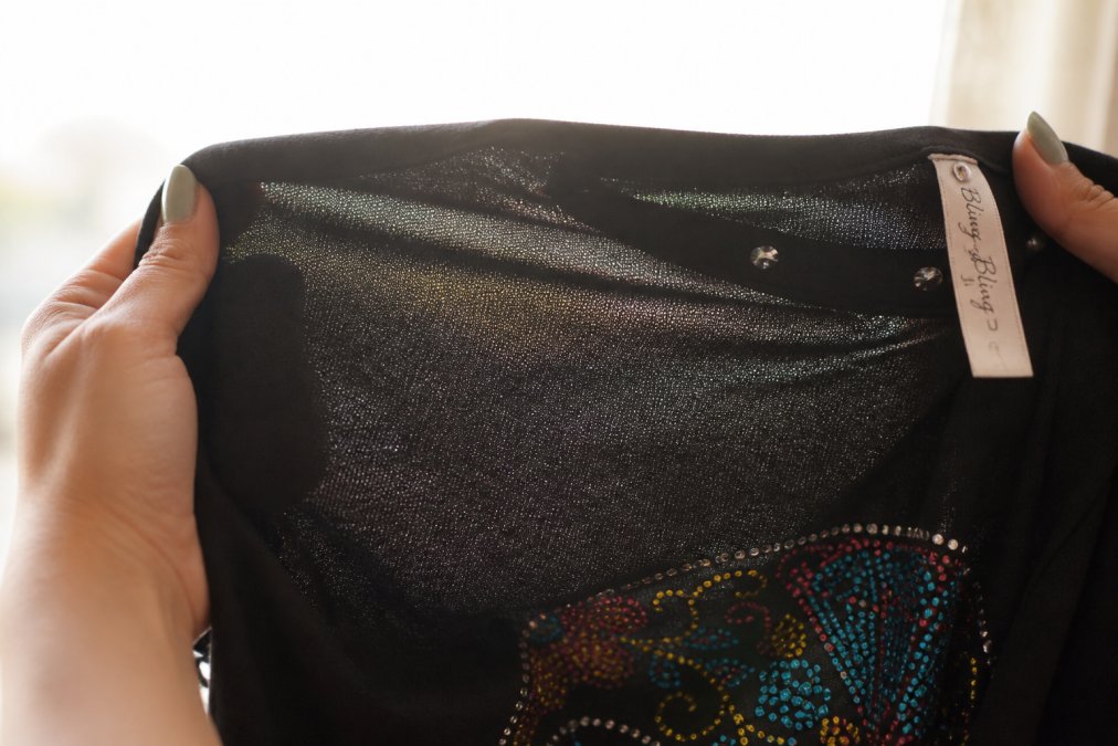 Close-up of hands holding a fabric swatch against natural light, showing weave texture and transparency, with a product tag visible at the edge