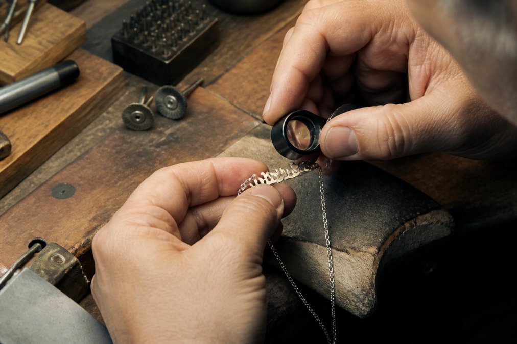 Jeweler inspecting a solder joint on a personalized jewelry name necklace under a magnifying loupe