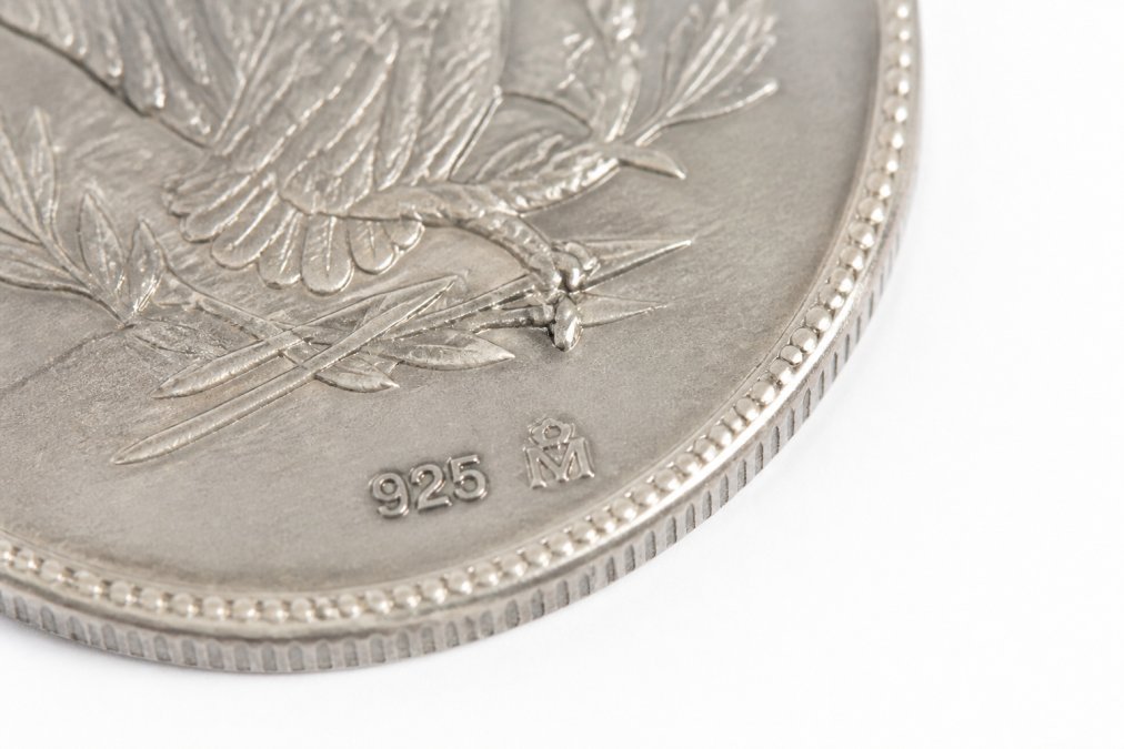 Close-up of a genuine silver coin showing crisp 925 hallmark and maker's mark stamps under bright studio lighting on white background