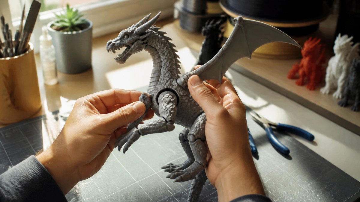 Close-up of hands holding and examining an articulated 3D-printed dragon figure, inspecting joints and surface details under bright natural window light