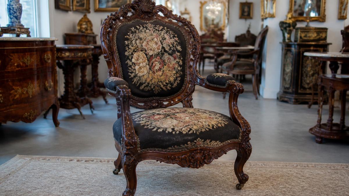Dark walnut Victorian parlor chair with carved crest and floral upholstery in an antique showroom
