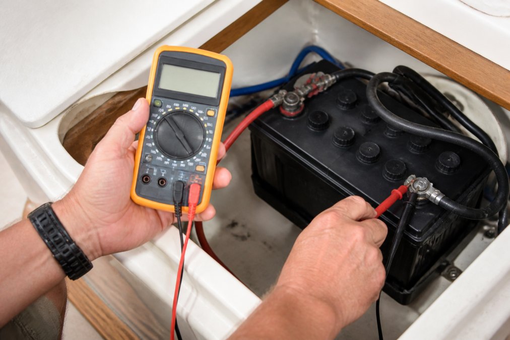 Hands using a digital multimeter to test boat battery voltage by touching the positive and negative terminals