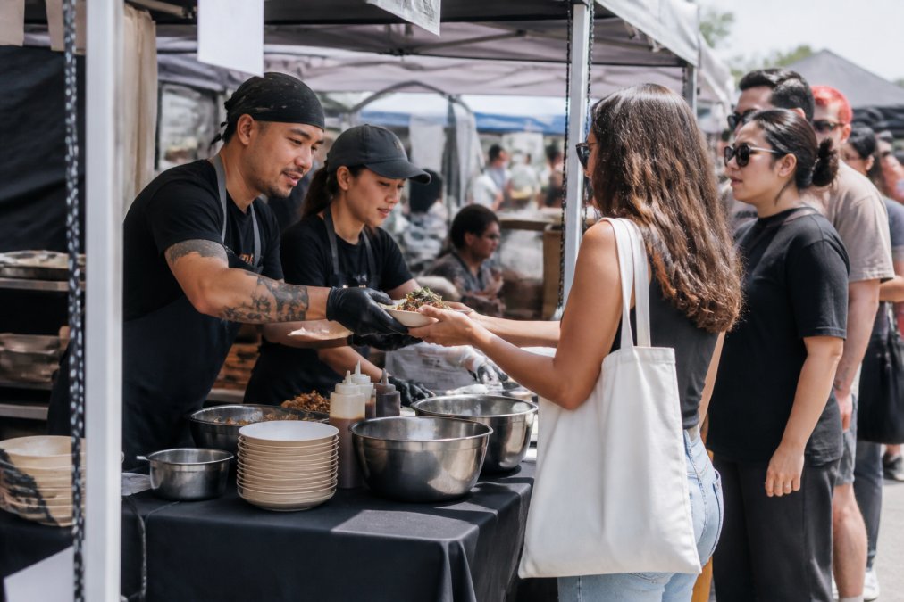 Chef and server at a busy outdoor pop-up food stall testing a restaurant concept for waiting customers