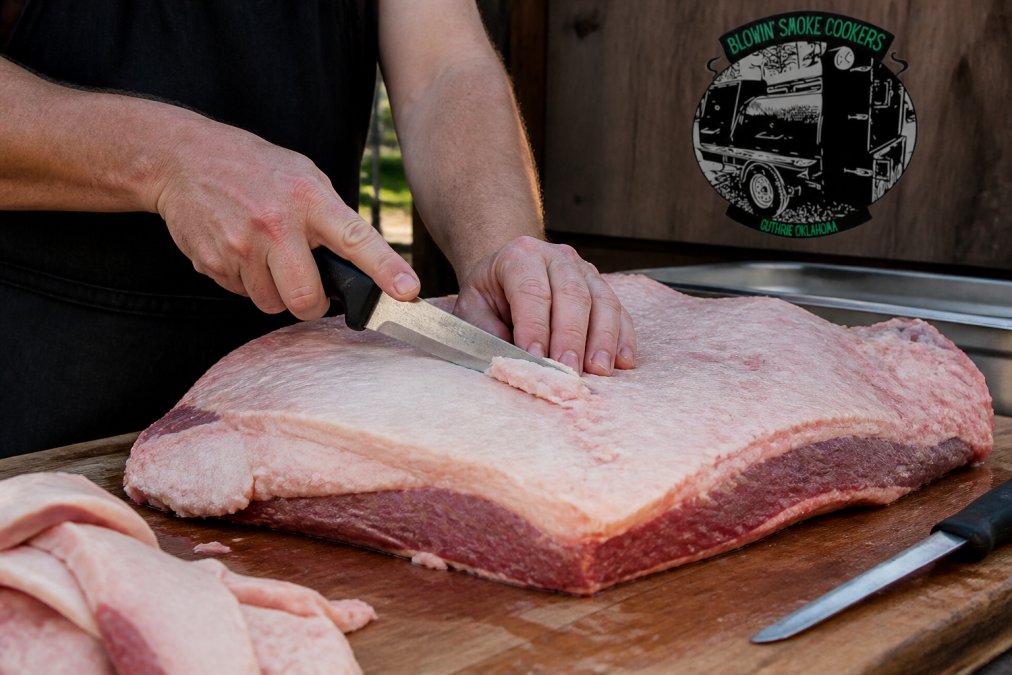 Pitmaster using a sharp boning knife to trim brisket fat in an outdoor prep area