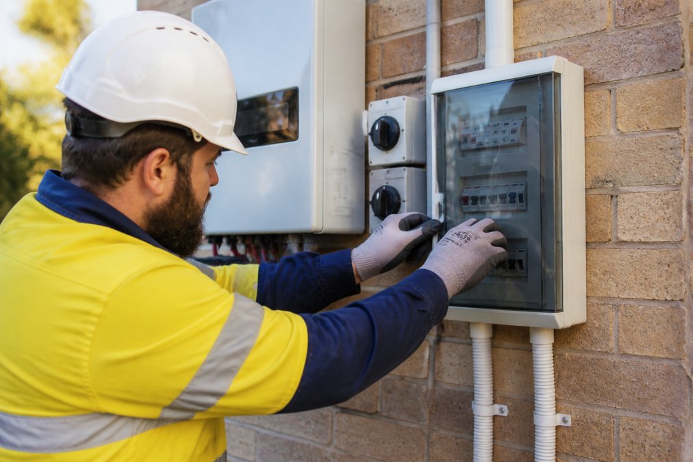 Technician's hands checking AC/DC disconnect switches and circuit breaker panel mounted near solar inverter installation in afternoon light