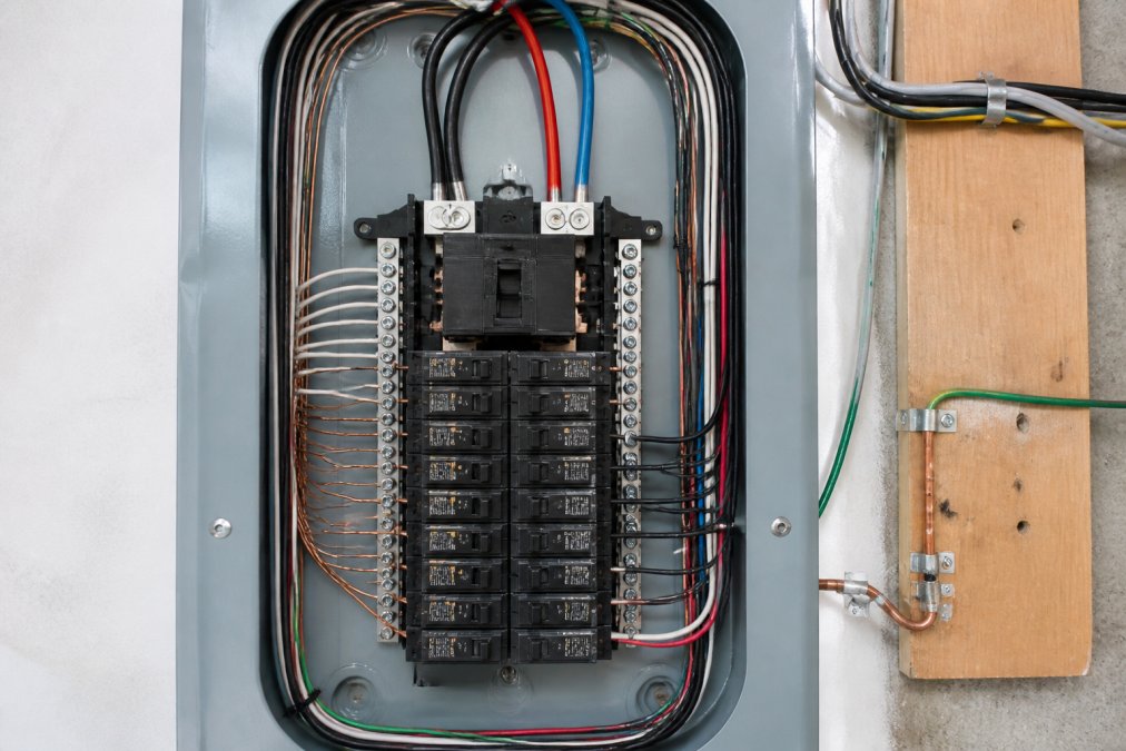 Close-up of a properly labeled breaker box showing main breaker, individual circuit breakers, grounding electrode connection, and service entrance conductors clearly organized and color-coded in a residential installation