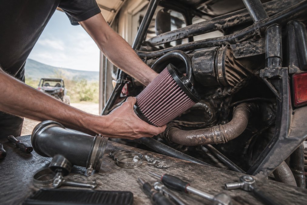 Rider installing an aftermarket air intake to boost UTV engine performance in a sunlit garage workshop